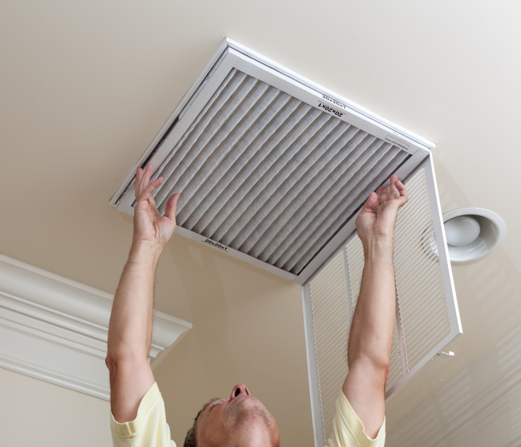 Male reaching up to open filter holder for air conditioning filter in ceiling