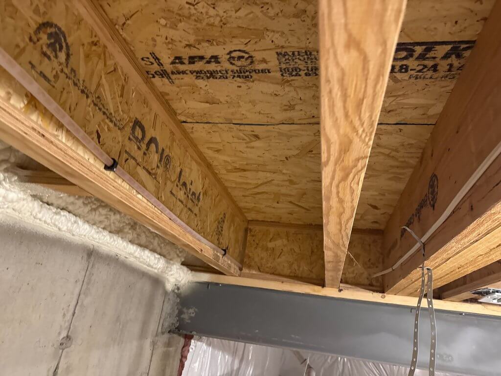 Underside view of floor framing showing joists and subfloor where homeowners can tighten connections to stop squeaky floors.