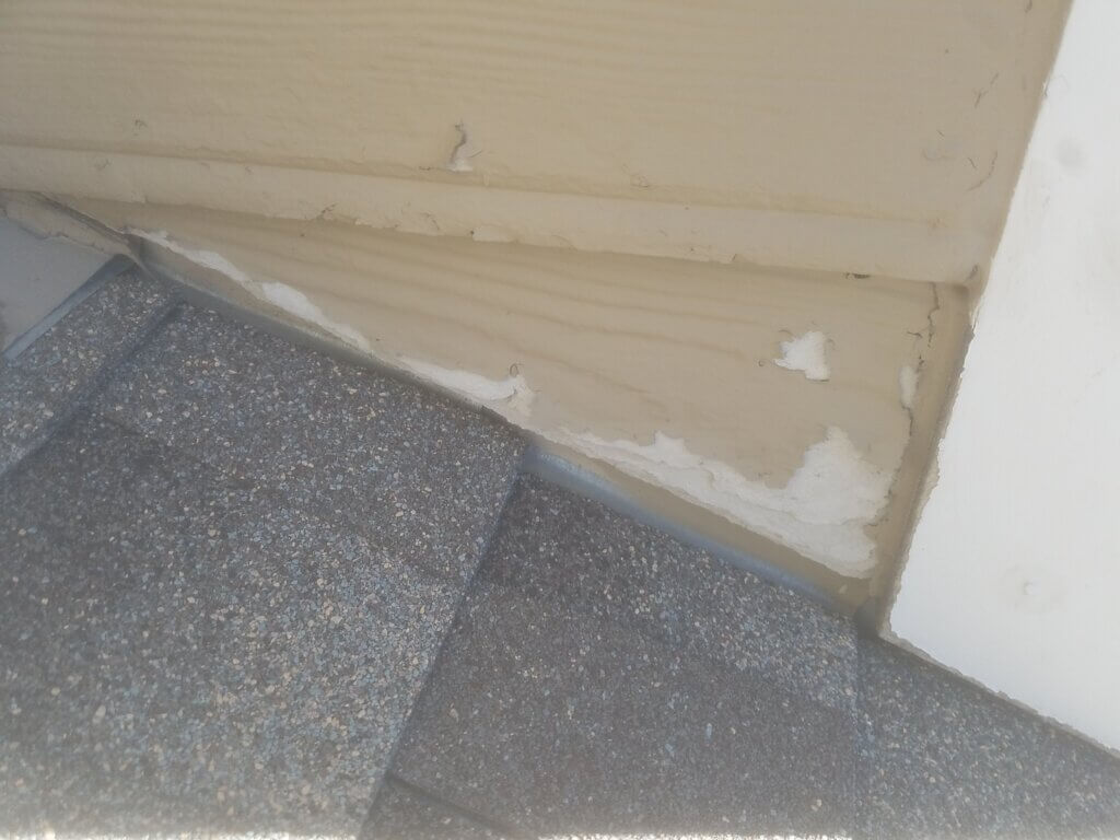 Water-damaged siding board next to roof shingles with visible staining and deterioration from moisture.