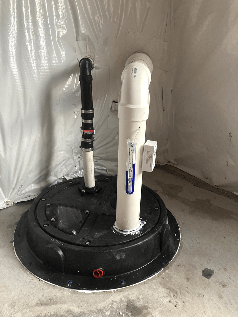 Radon mitigation system in a Denver home basement with PVC vent pipe and manometer gauge installed for active soil depressurization.